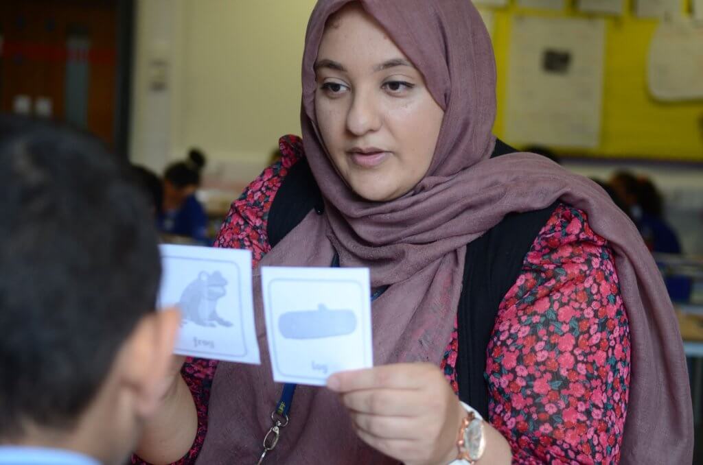 A teacher holding up word-picture cards, with labelled images of a frog and a log.