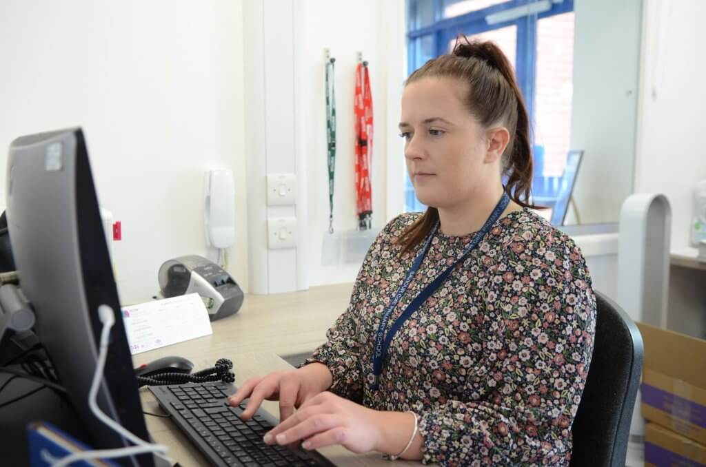 A woman sitting at a computer desk in the school office.