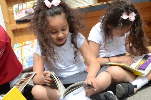 Two girls sitting on the floor, reading books in their laps.