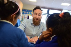 A teacher sitting at a desk with two pupils in the classroom.