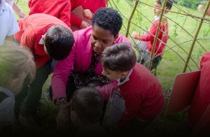 A teacher and pupils look down at what they find in the school gardens.