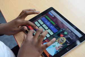 Close up of a child's hands typing on an iPad screen, playing an online learning game.