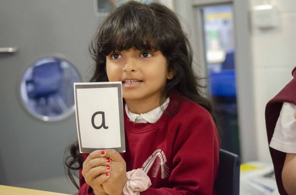 A girl in Early Years holding up a sign with the letter 'a.'