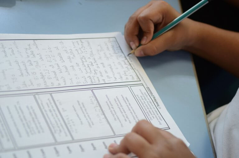 A child's hand holding a pen and filling in a worksheet.