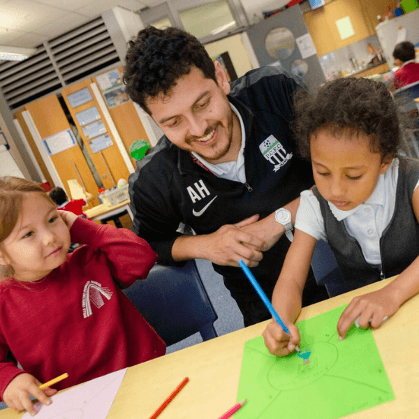 Teacher helps two early years pupils with their drawings. 
