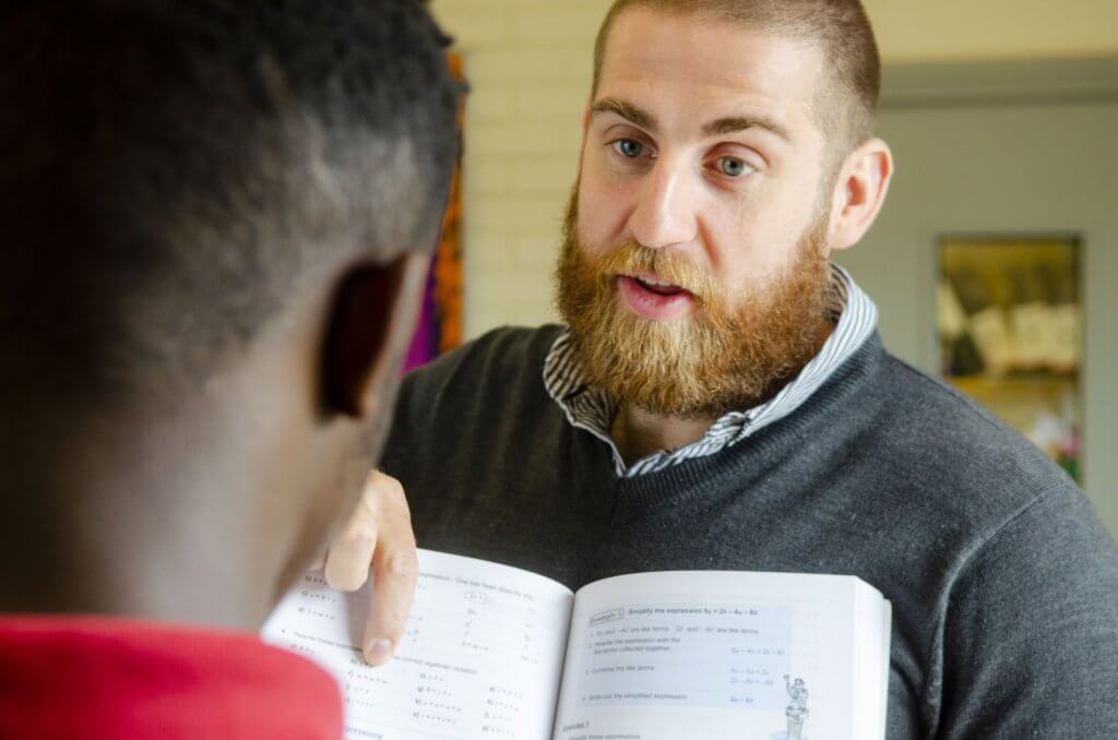 A teacher holding open a book and showing the page to a pupil.