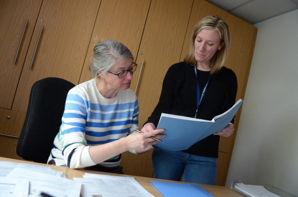 Two members of staff in conversation as they look over documents in the school office.