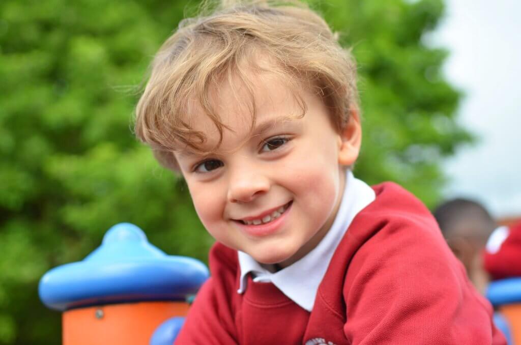 A young school boy in the playground smiling.