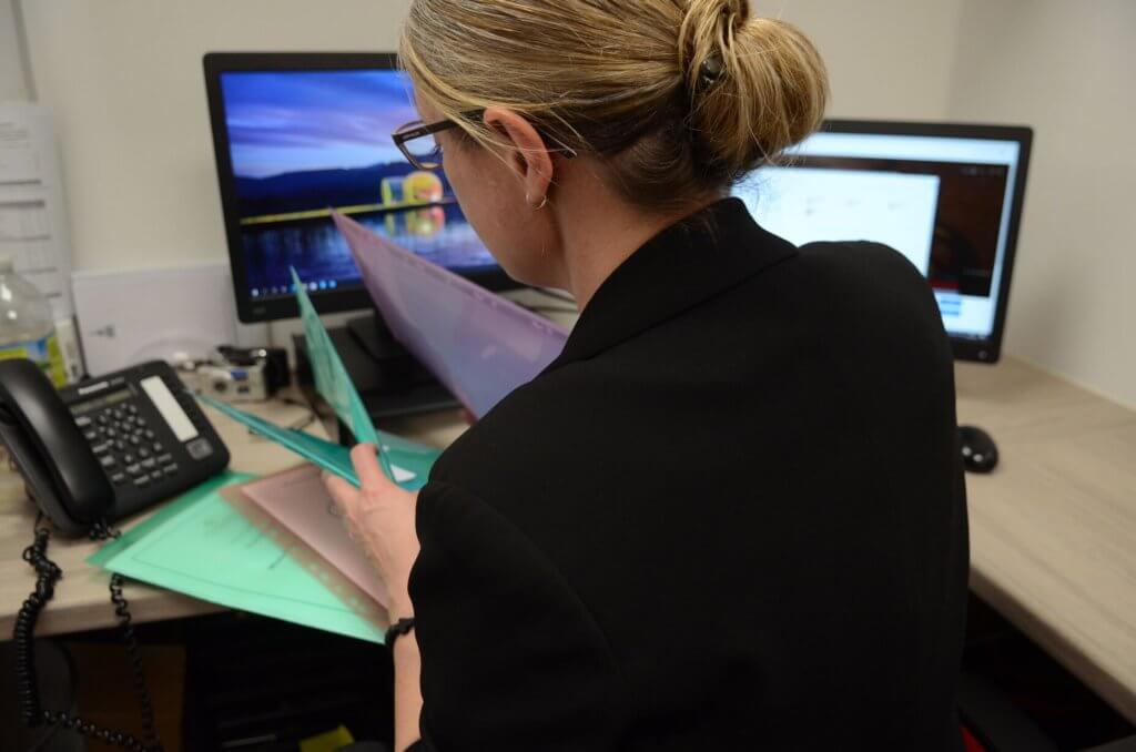 A woman looking through files whilst sitting at a computer in the office.