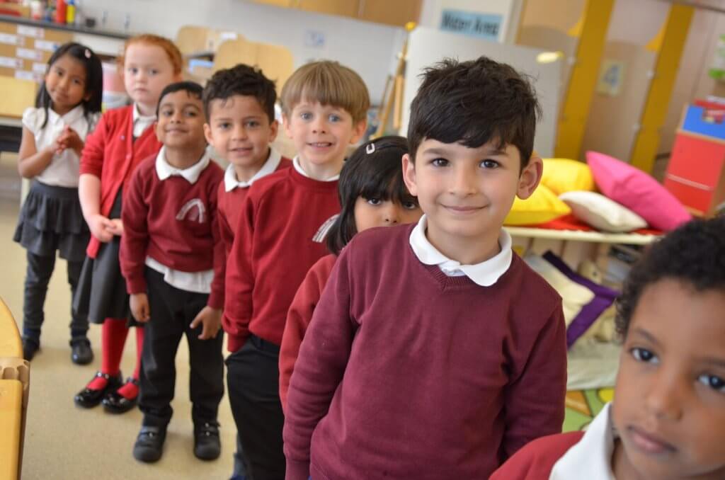Children in the early years classroom lined up and smiling at the camera.