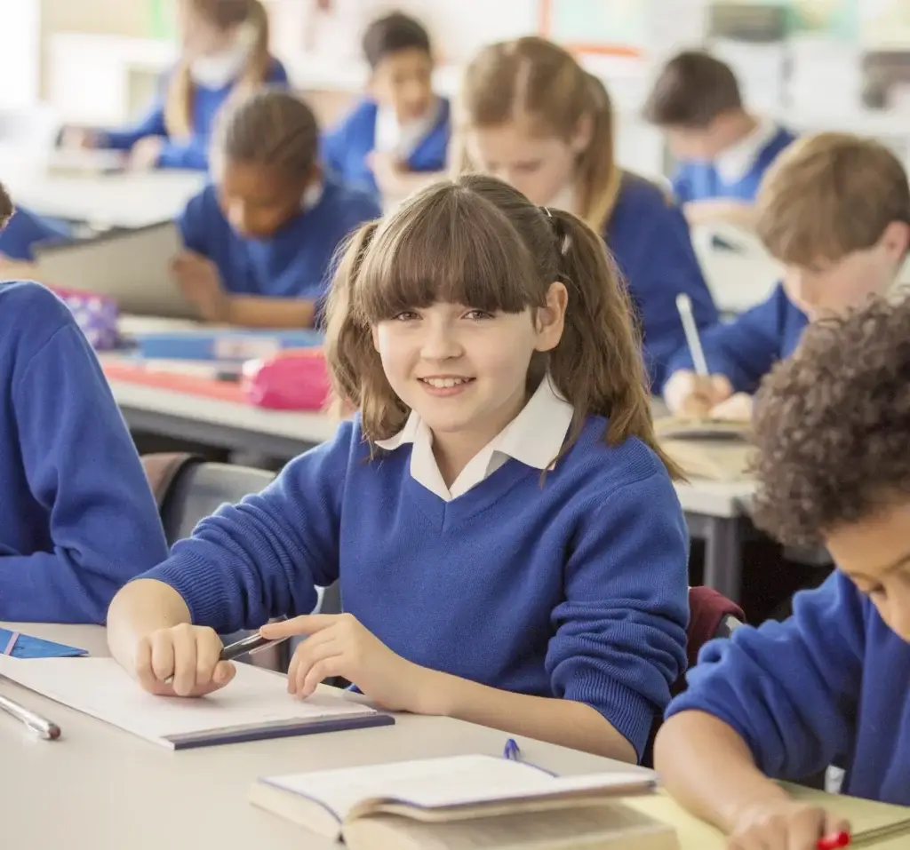 female pupil looks up from desk smiles at camera